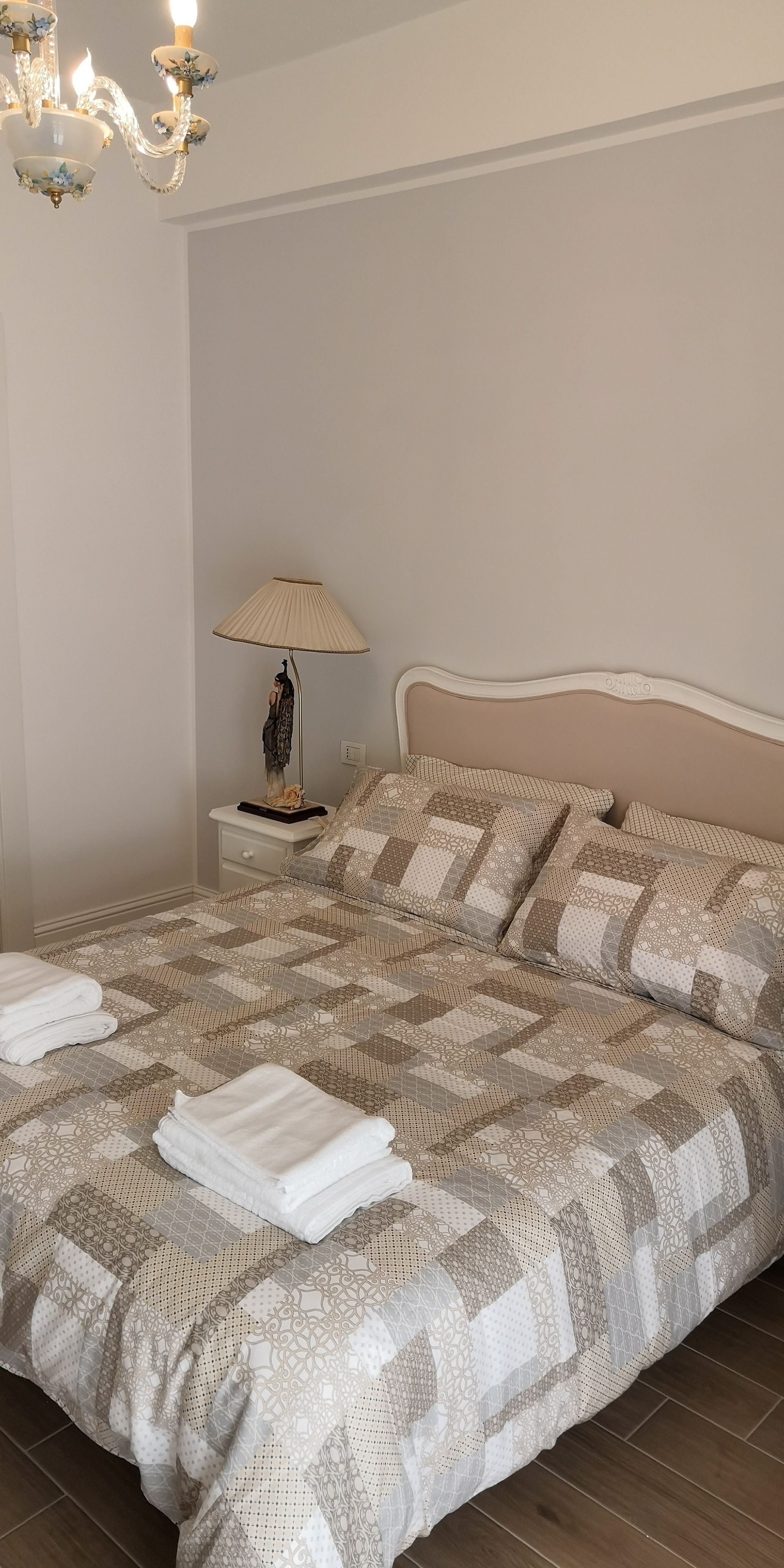 A neatly made bed with a patterned bedspread, a bedside lamp, and a nightstand with a decorative item.