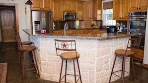A kitchen with wooden cabinets, a stone island, and bar stools. - The Silver Spur Resort - Campsite (Canton)