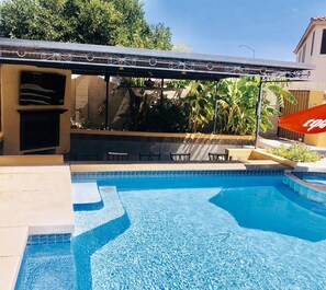 Una piscina con bordo piastrellato, un'area relax coperta e una bandiera rossa con scritta bianca.