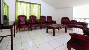 A living room with a green curtain, a television, and a coffee table. - Wisma Lamida 2 Syariah (Jakarta)