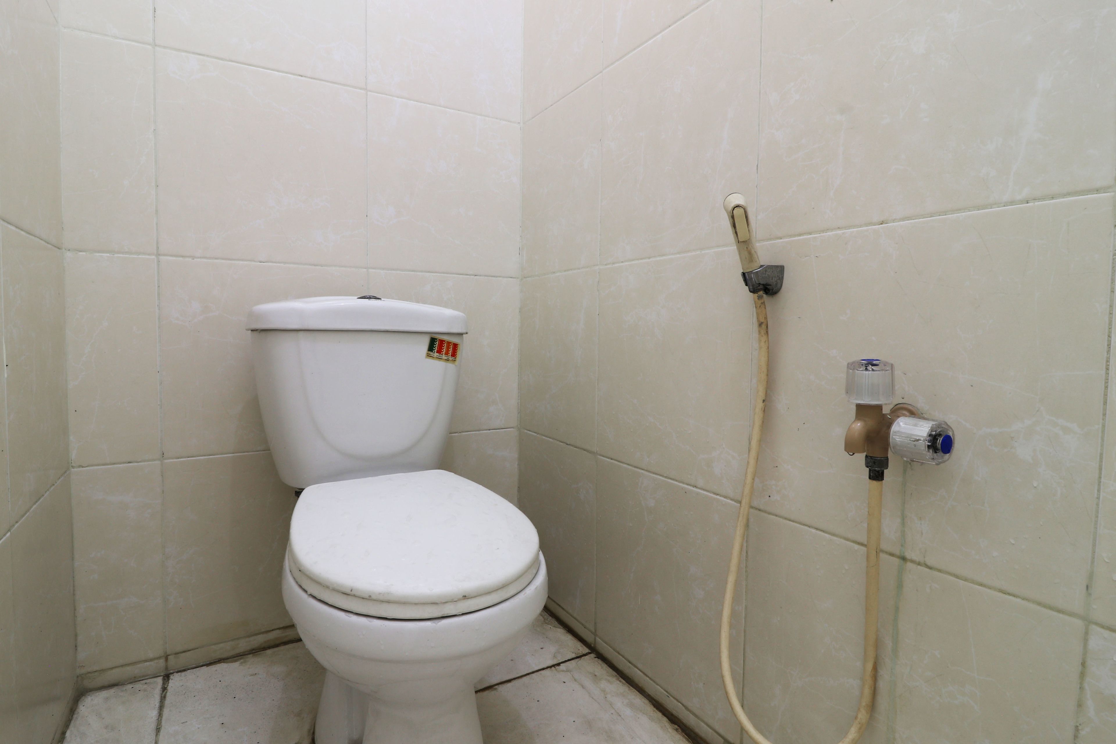 A small, basic bathroom with a toilet and a water faucet on the wall.