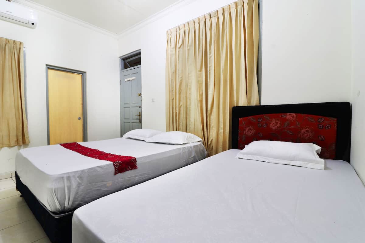 A hotel room with two single beds, beige curtains, and a red floral headboard.