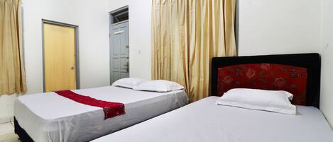 A hotel room with two single beds, beige curtains, and a red floral headboard.