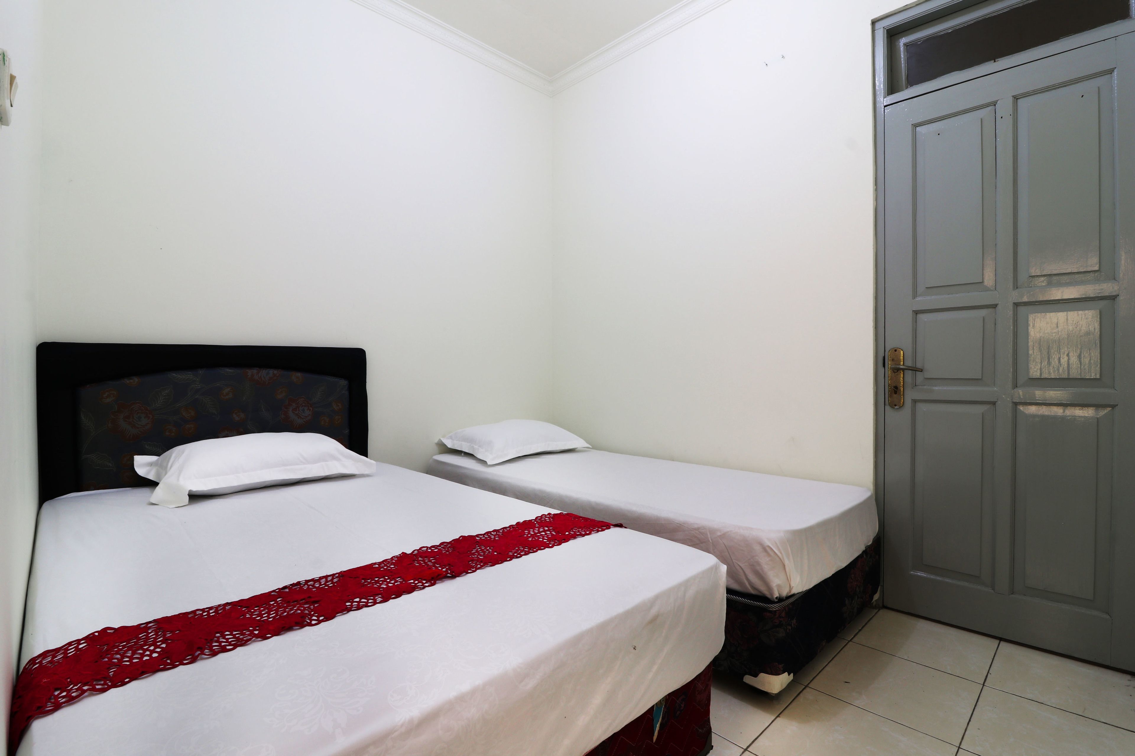 A room with two single beds, a grey door, and a tiled floor.