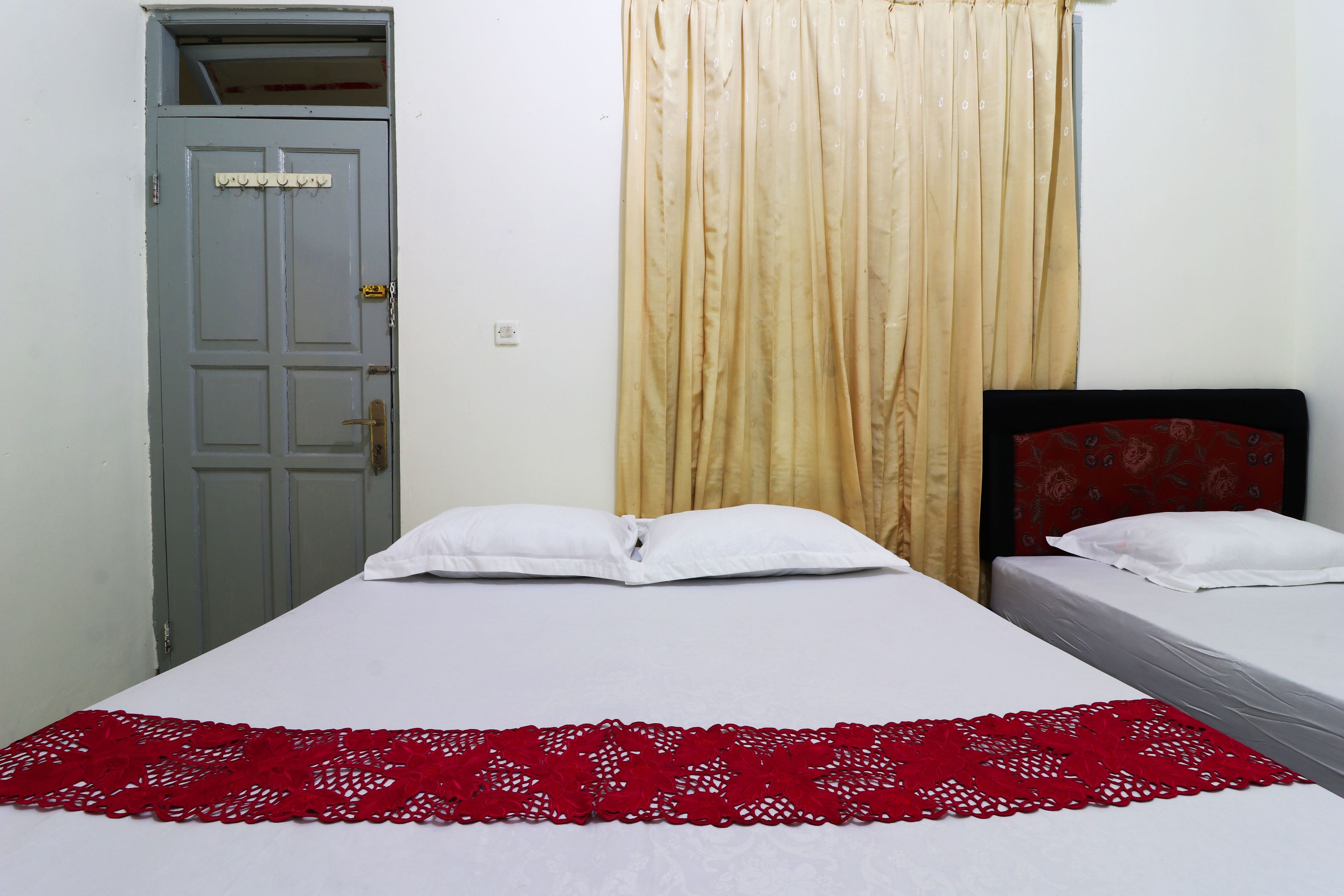 A room with two beds, a grey door, and a beige curtain.