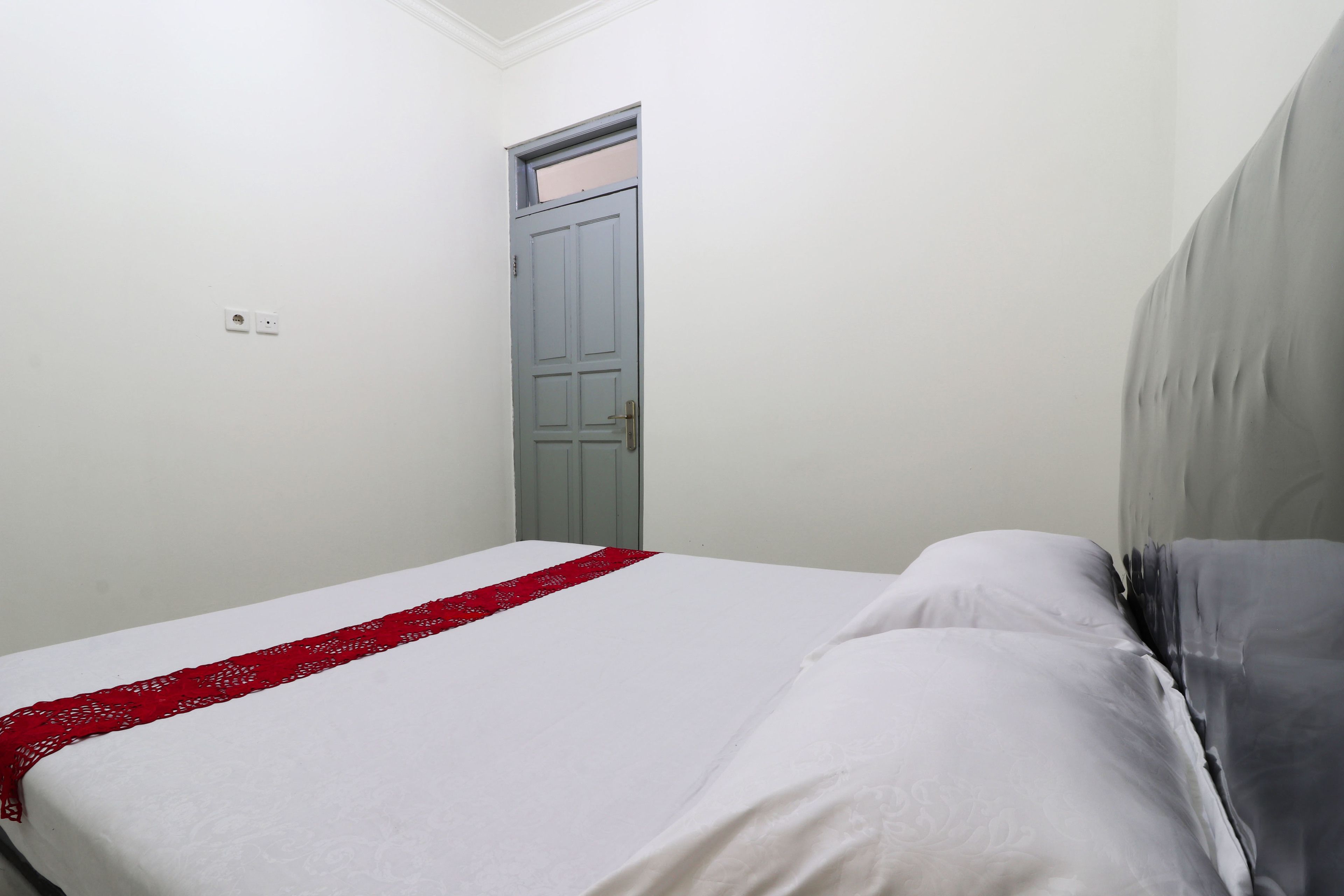 A bedroom with a bed, a door, and a light switch on the wall.