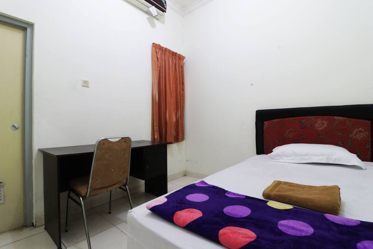 A small, clean room with a bed, a desk, and a chair.