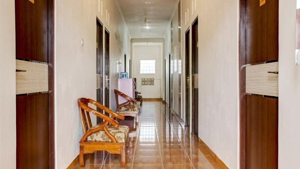 A hallway with wooden doors, a tiled floor, and a row of wooden chairs with cushions. - Semata Wayang Syariah Homestay (Banjarbaru)
