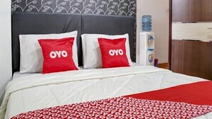 A hotel room with a bed, two pillows with 'OYO' branding, a patterned wall, a water dispenser, and a wooden wardrobe. - Semata Wayang Syariah Homestay (Banjarbaru)