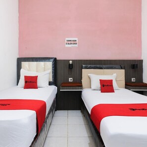 Ein Hotelzimmer mit zwei Betten, jeweils mit einer roten Decke und einem roten Kopfkissen, und einem an der Wand befestigten Schild.