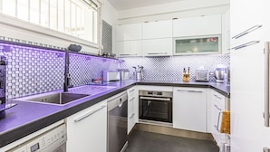 A modern kitchen with white cabinets, a black countertop, and a purple-lit backsplash. - Apartment Eze Seaside in 1st line facing the sea (Èze)