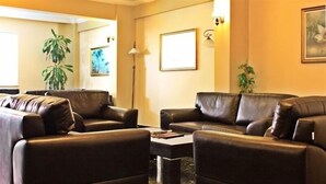 A living room with two leather sofas, a coffee table, and a floor lamp. There are framed pictures on the wall and a potted plant.
