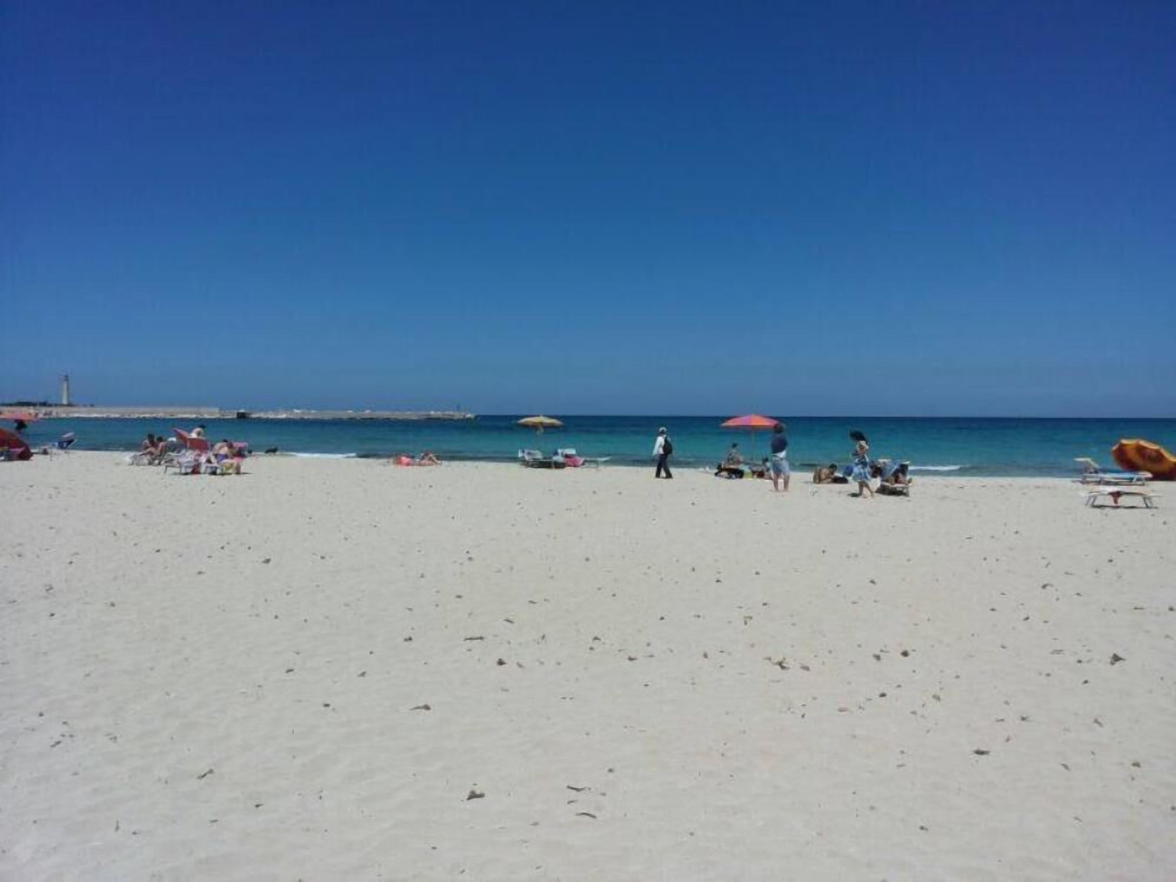 Una playa con arena blanca, sombrillas y gente.