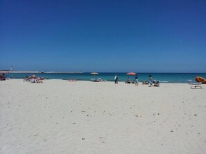 Uma praia com areia branca, guarda-sóis e pessoas.