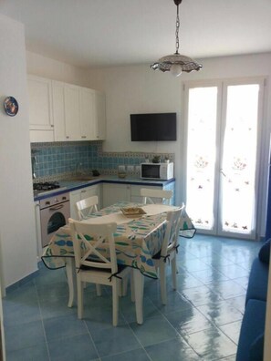 A compact kitchen with white cabinets, a microwave, and a dining table with chairs. - "AFRODITE" APARTMENT ONLY 250 MT FROM THE SEA (San Vito Lo Capo)