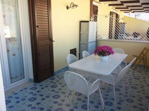 A dining area with a white table and chairs, a potted plant, and a tiled floor. - "AFRODITE" APARTMENT ONLY 250 MT FROM THE SEA (San Vito Lo Capo)