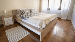 A bedroom with a wooden bed, a bedside table with a lamp, and a striped rug. - Desire City Center Apartment Terazije (Belgrade)