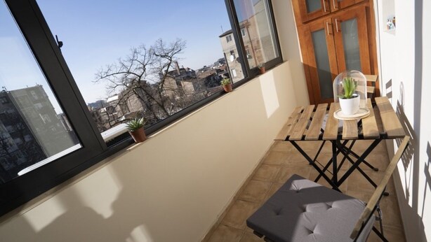 A balcony with a view of the city, a small table with a cushion, and a potted plant. - Desire City Center Apartment Terazije (Belgrade)