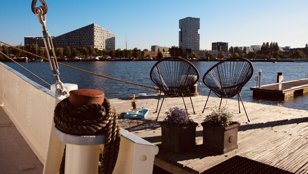 En træterrasse med to sorte metalstole, en potteplante og en flaske champagne på en båd.