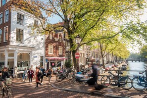 Une scène de rue avec des piétons, des vélos et des voitures garées le long d’un canal.