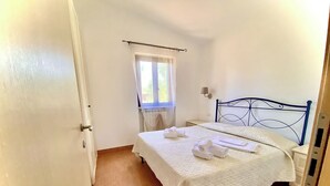 A bedroom with a bed, a nightstand, a window with a curtain, and a wall-mounted lamp. - Apartment "semi-detached Villa" for 5/6 person on the ground floor with separate entrances and with square meters 150 private Garden with Barbecue and Sunbeds (Vieste)