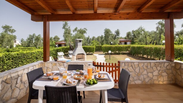 An outdoor dining area with stone walls, wooden furniture, and a view of a landscaped garden. - Apartment "semi-detached Villa" for 5/6 person on the ground floor with separate entrances and with square meters 150 private Garden with Barbecue and Sunbeds (Vieste)