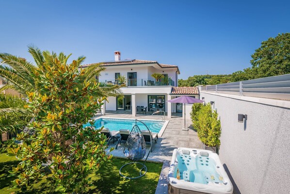 Ein modernes Haus mit Schwimmbad, Sitzgelegenheiten im Freien und Whirlpool.