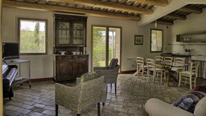 A spacious room with a piano, wicker chairs, a dining table with chairs, and a kitchen area. - Fully private fenced villa with pool – ideal for families, pet friendly (Ostra)