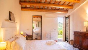 A bedroom with a bed, bedside table, lamp, wooden ceiling beams, and a view of the outdoors. - Fully private fenced villa with pool – ideal for families, pet friendly (Ostra)