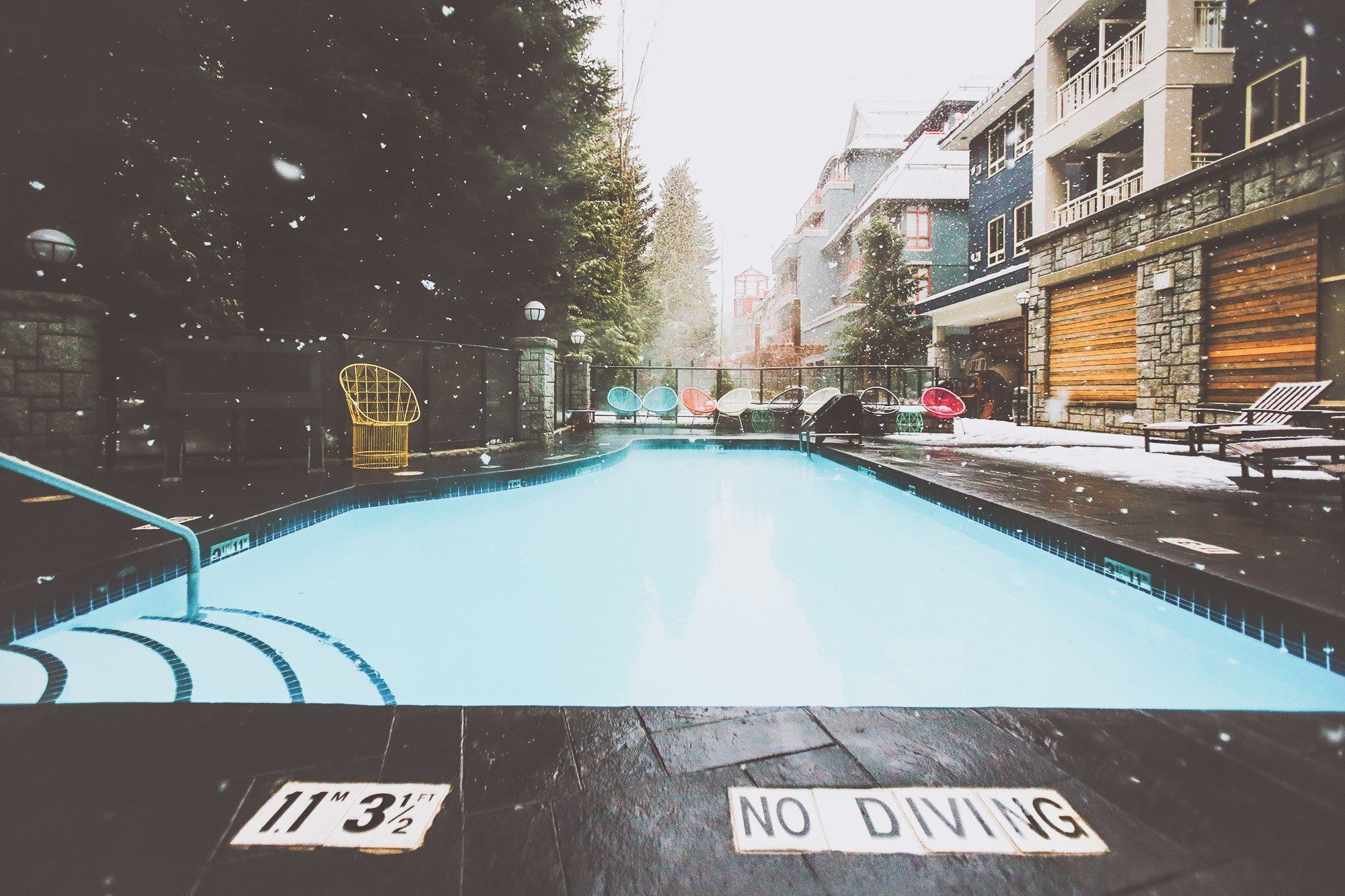 Una piscina amb un senyal de 'NO DIVING', envoltada d'edificis i mobiliari exterior.