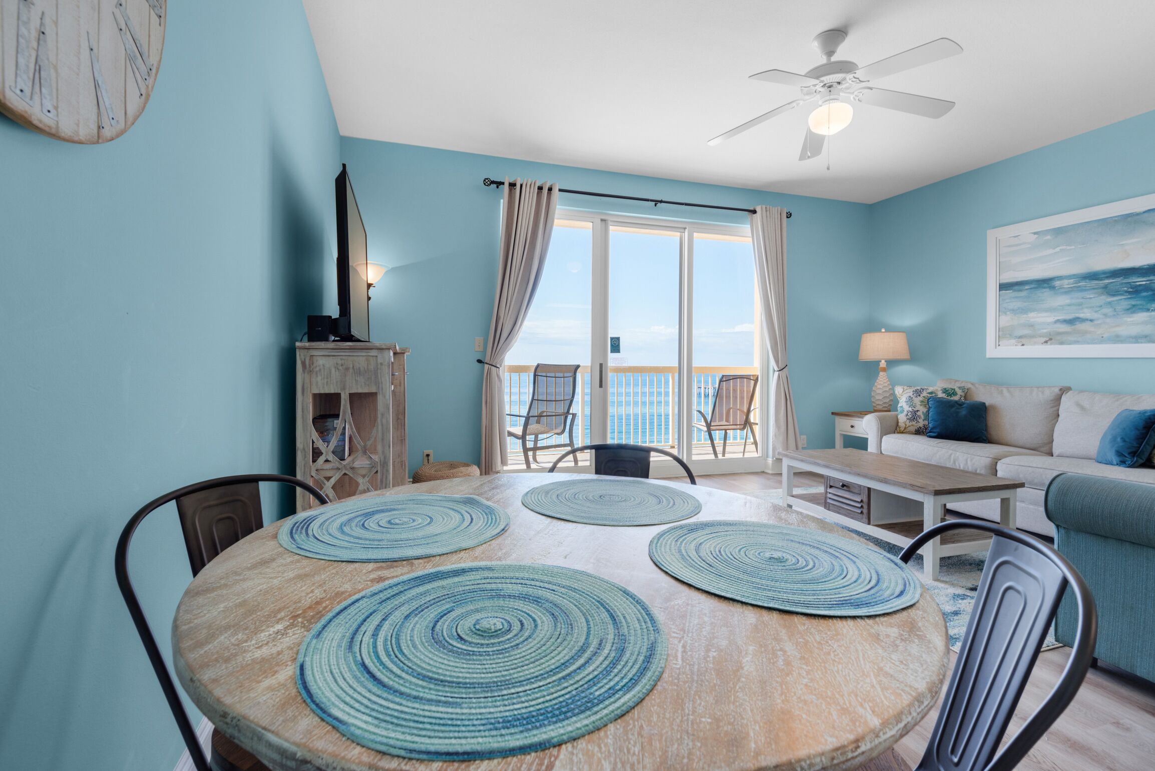 A dining area with a round table, four blue and white woven placemats, and a ceiling fan.