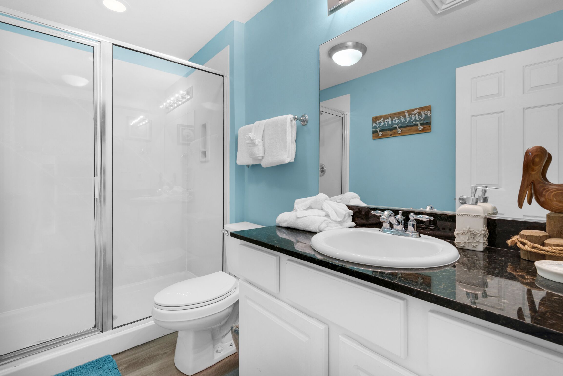 A modern bathroom with a glass shower enclosure, white toilet, and a vanity with a black countertop and white sink.