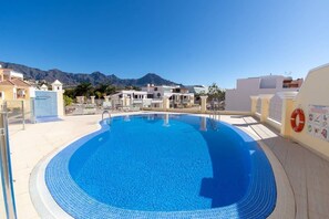 A swimming pool with a clear blue water, surrounded by buildings and mountains in the background.