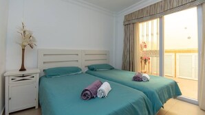 A hotel room with two beds, a nightstand, and a view of a balcony. - Bahia la Caleta 1 - Two Bed (La Caleta)