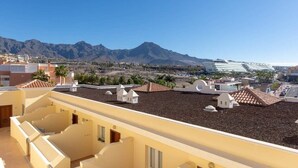 A rooftop terrace with a view of mountains, featuring multiple buildings with flat roofs and a clear sky. - Bahia la Caleta 1 - Two Bed (La Caleta)
