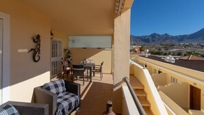 A balcony with a sofa and table, a view of mountains, and a clear sky. - Bahia la Caleta 1 - Two Bed (La Caleta)