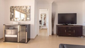 A modern living room with a glass cabinet, a flat-screen TV, and a dark wooden cabinet. - Bahia la Caleta 1 - Two Bed (La Caleta)