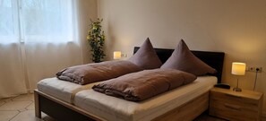 A double bed with two pillows, a bedside table with a lamp, and a window with curtains.