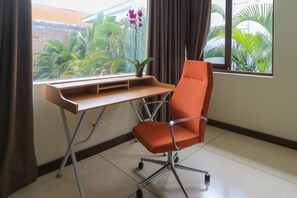 A workspace with a desk and an orange office chair, a potted plant, and a view of greenery through a window.