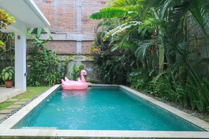 A swimming pool with a pink flamingo float, surrounded by lush greenery and a brick wall in the background. - Villa Soulange (Canggu)