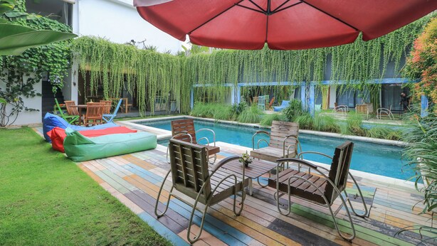 A poolside area with a wooden deck, a red umbrella, and hanging greenery. - Base Guesthouse and Hostel (Canggu)