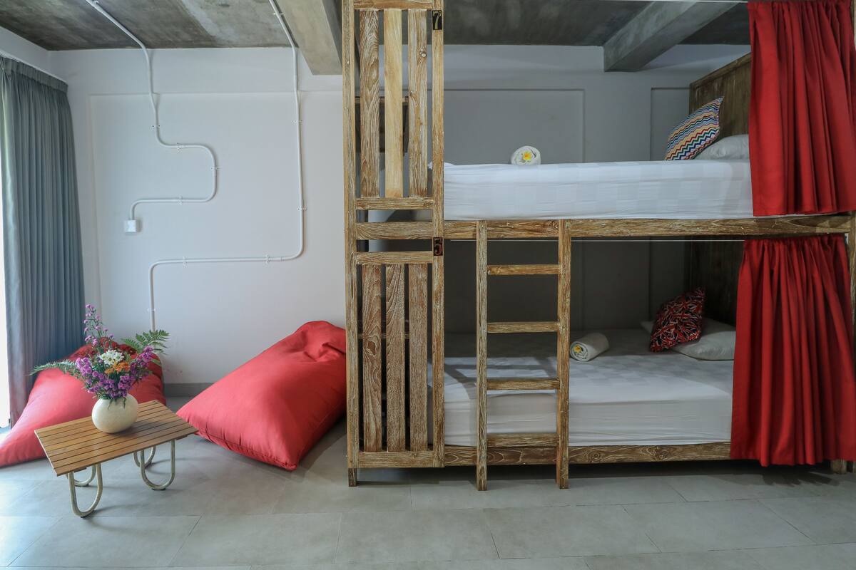 A bunk bed with a wooden frame, a small table with a vase, and red pillows.