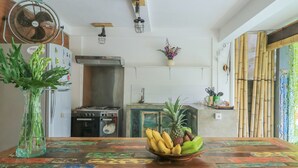 A kitchen with a wooden table, a fan, a refrigerator, and a stove. - Base Guesthouse and Hostel (Canggu)
