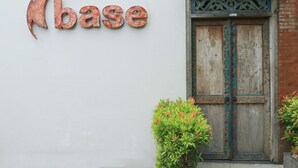 A building with a rustic wooden door and a wall-mounted sign spelling "base". - Base Guesthouse and Hostel (Canggu)