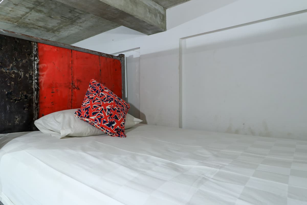 A bed with white bedding and a red and blue patterned pillow.