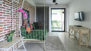 A room with a bed, a TV, a desk, and a balcony with a view. - Base Guesthouse and Hostel (Canggu)