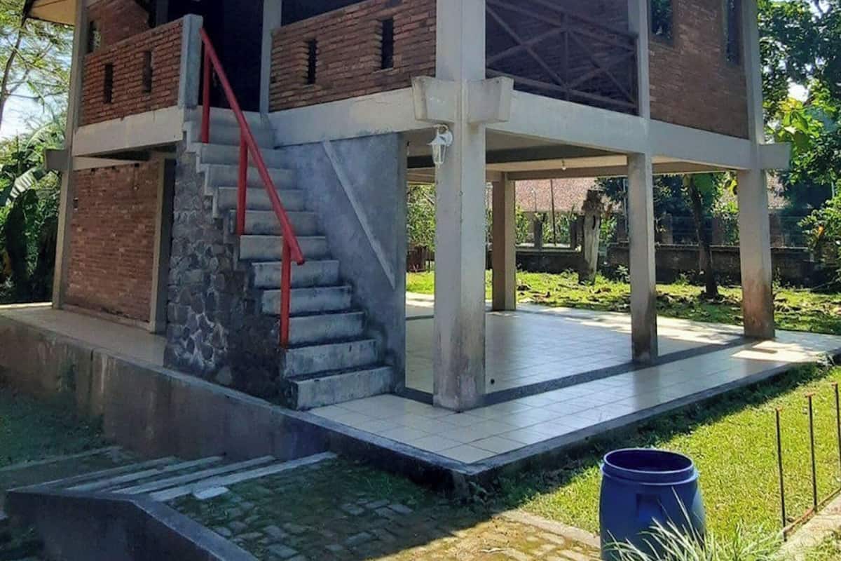 A two-story building with a sloped roof, a staircase with red railings, and a covered outdoor area.
