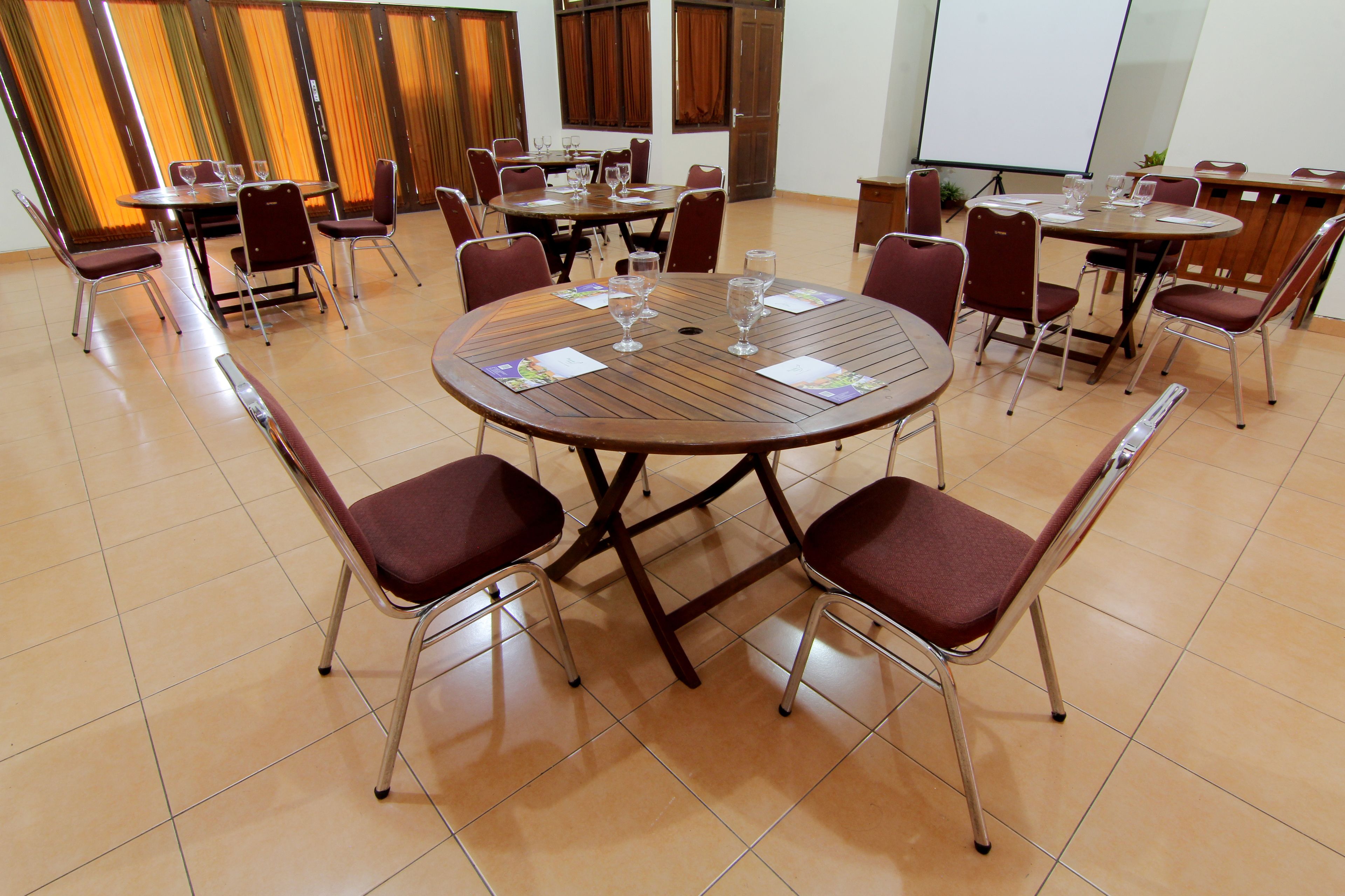Un salón de conferencias con mesas y sillas redondas, una pantalla de proyector y una zona para presentaciones.
