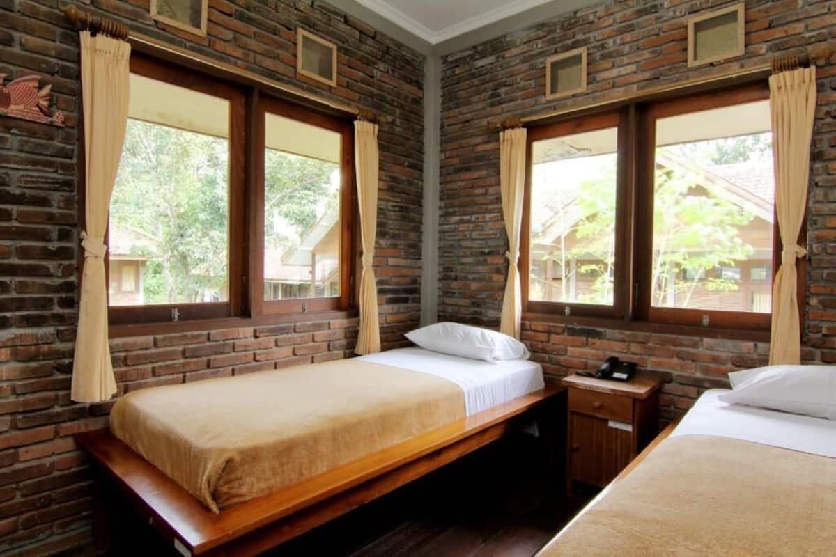 A room with a brick wall, two beds, a nightstand, and a window with curtains.
