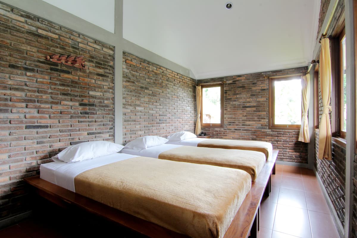 A room with two beds, a brick wall, a window, and a wooden bench.